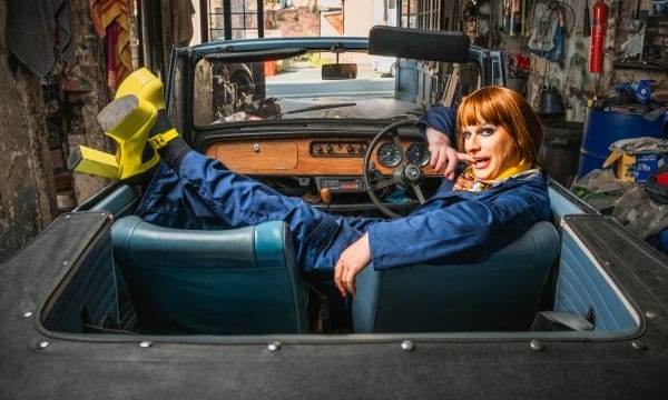 A car mechanic wearing blue overalls sat across the seats of a shell of a car