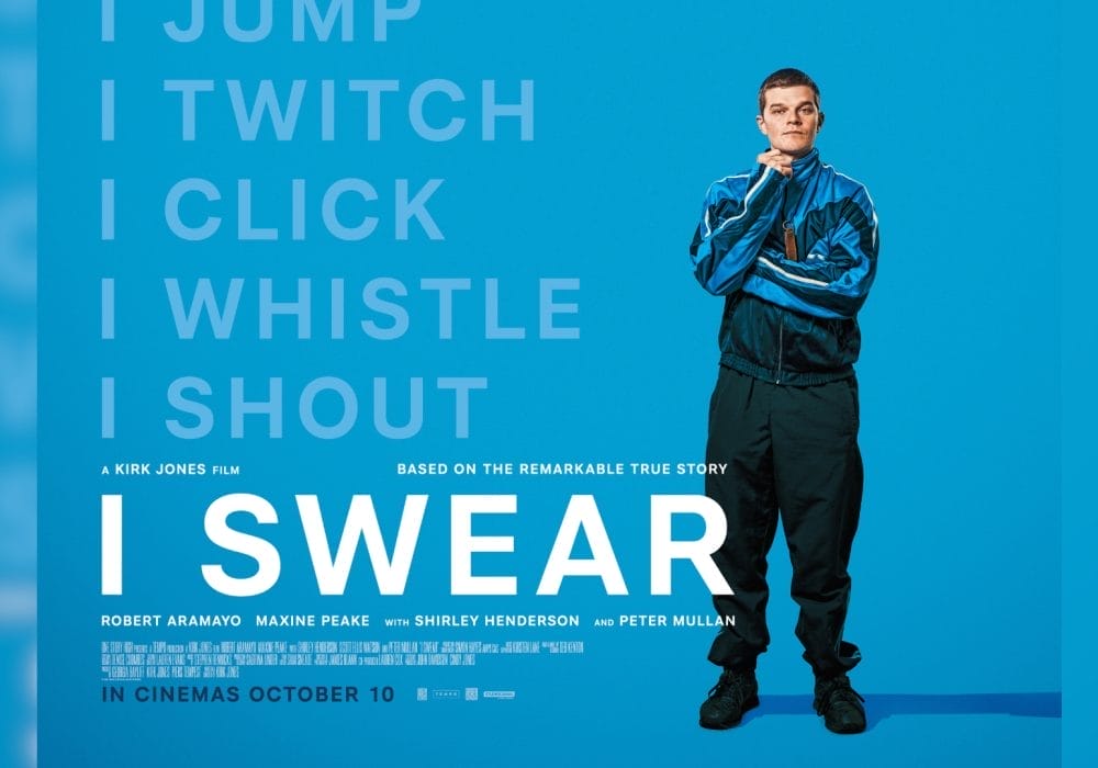 A young man with short hair wearing a blue and black tracksuit stands confidently resting a closed hand on his chin