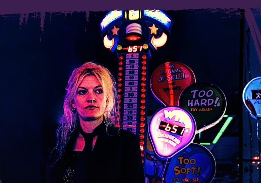 A blonde haired woman dressed in black standing in front of Las Vegas style neon lighting