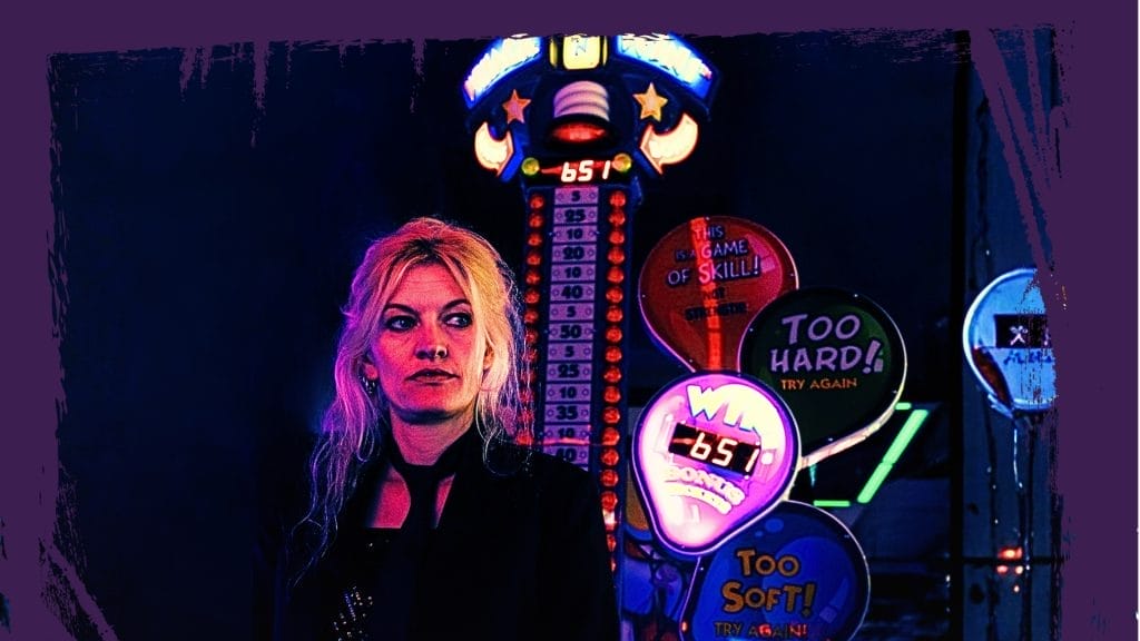 A blonde haired woman dressed in black standing in front of Las Vegas style neon lighting