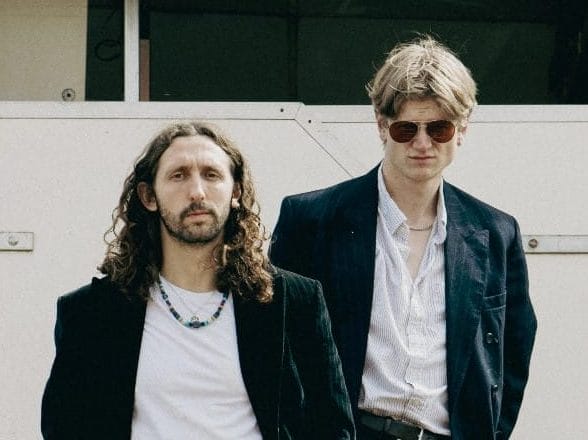 Two male musicians wearing dark jackets looking moody