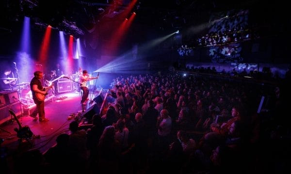 A lively band plays on stage, surrounded by bright lights that enhance the dynamic performance for the crowd.