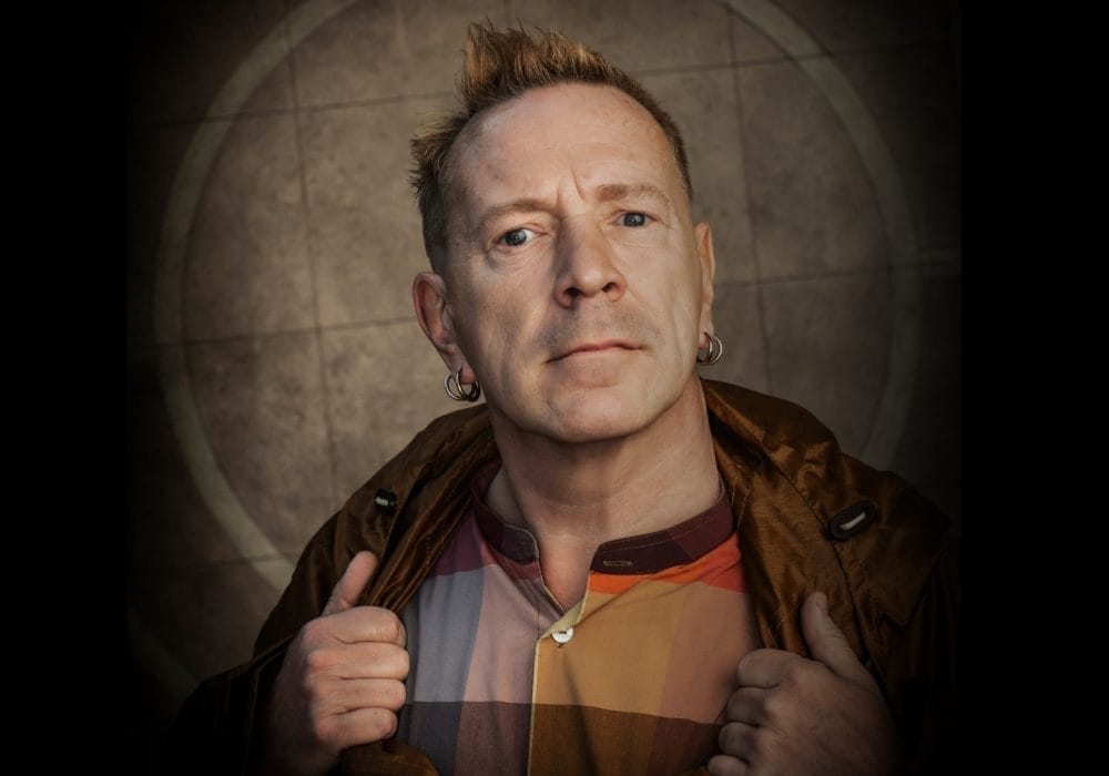 A quirky older man with spiky hair confidently looking directly at the camera