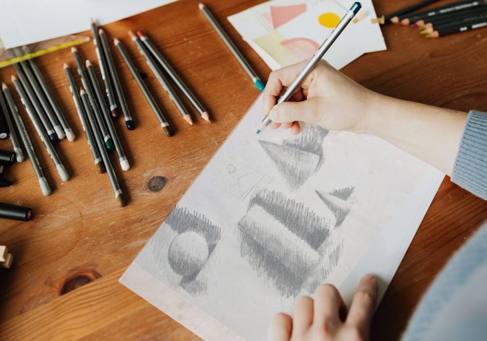 A person sketches on paper using a pencil, focused on their drawing technique and the details of the artwork.