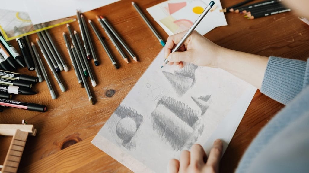 A person sketches on paper using a pencil, focused on their drawing technique and the details of the artwork.
