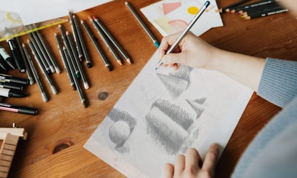 A person sketches on paper using a pencil, focused on their drawing technique and the details of the artwork.