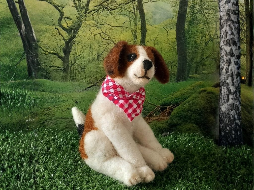 A dog made from felt wearing a bandana in a woodland setting