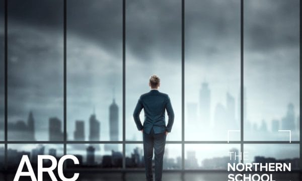 A man wearing a suit standing in front of a large window looking out at a cityscape