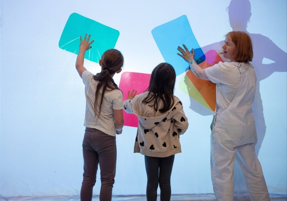 A female adult with 2 children making shapes with coloured sheets of paper