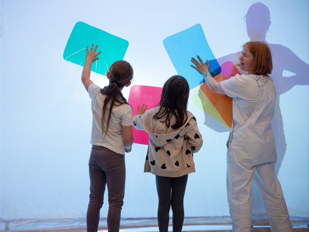 A female adult with 2 children making shapes with coloured sheets of paper